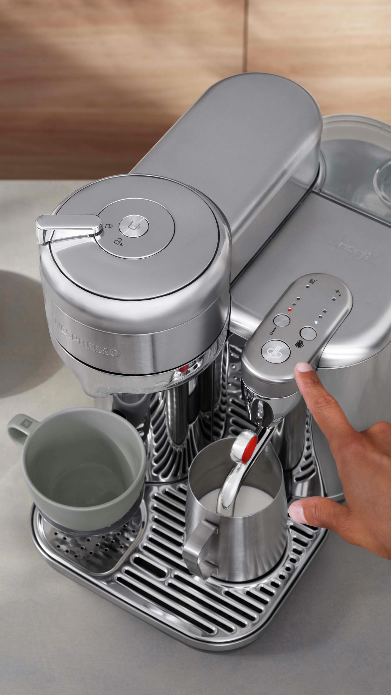 Silberne Nespresso-Kaffeemaschine mit Hand, die einen Knopf drückt.