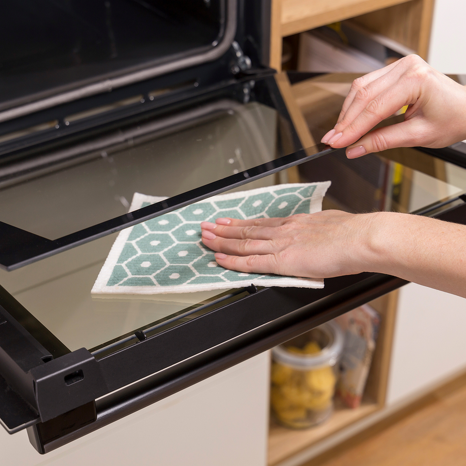 Een persoon maakt de binnenkant van een oven schoon. Een groen en wit patroon doek wordt gebruikt.