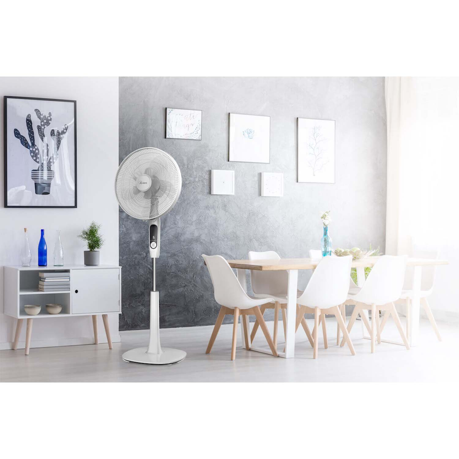 Un ventilatore bianco da terra è in una stanza con tavolo, sedie e arte. La stanza ha un'estetica moderna.