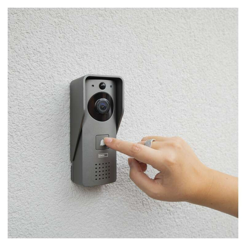 Egy személy keze megnyom egy gombot egy szürke csengőn egy texturált falon.