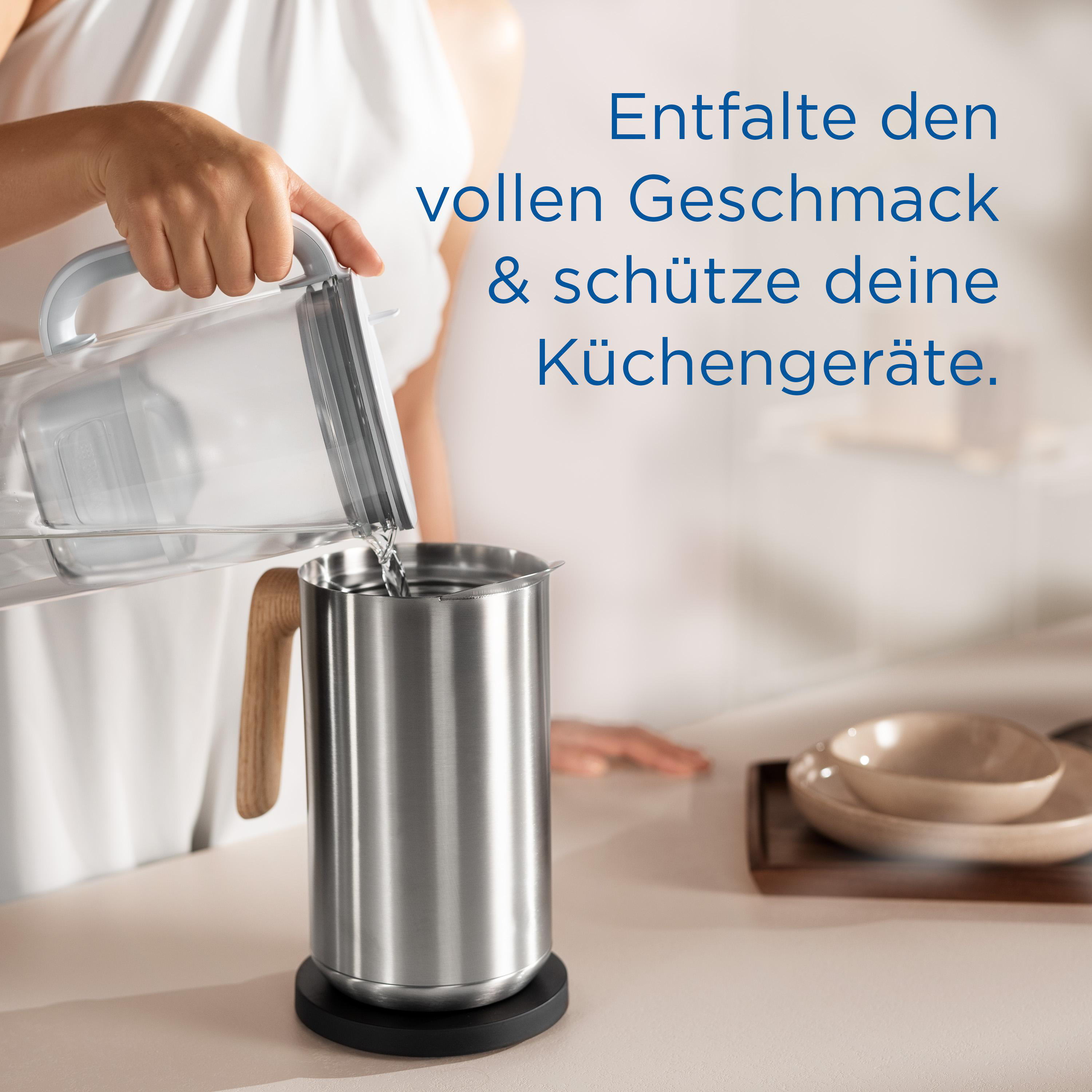 Eine Person gießt Wasser aus einem Krug in einen silbernen Behälter. Text ist sichtbar.