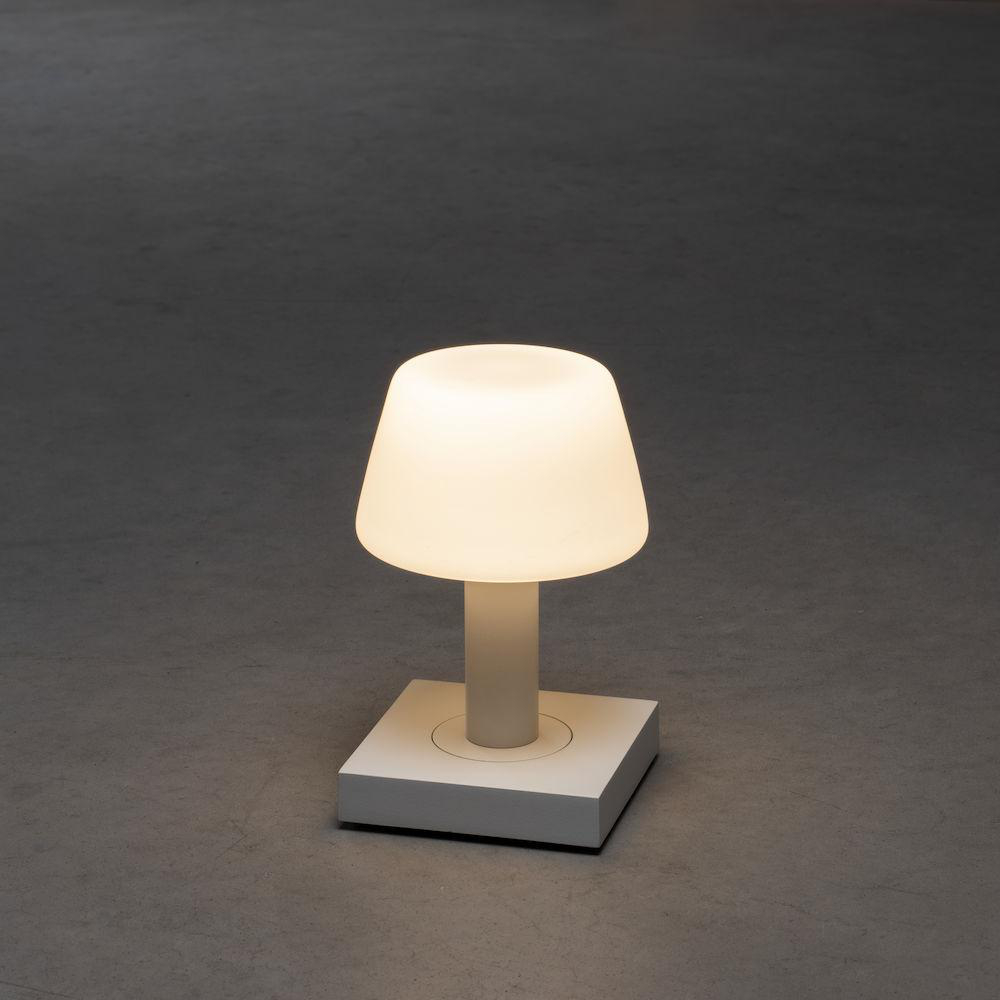 Eine weiße Tischlampe auf einem weißen quadratischen Sockel auf grauem Hintergrund.