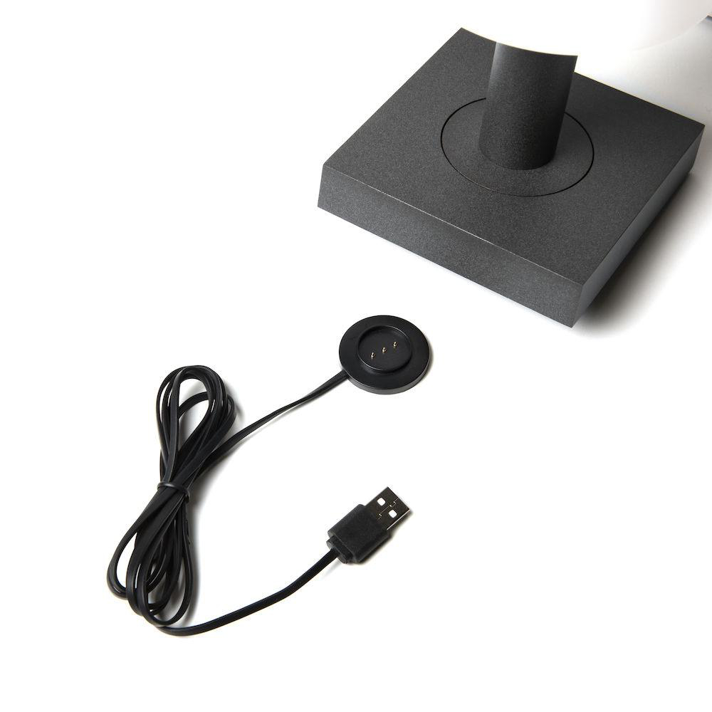 Schwarzes Ladekabel, Ladegerät und Basis auf weißer Oberfläche.
