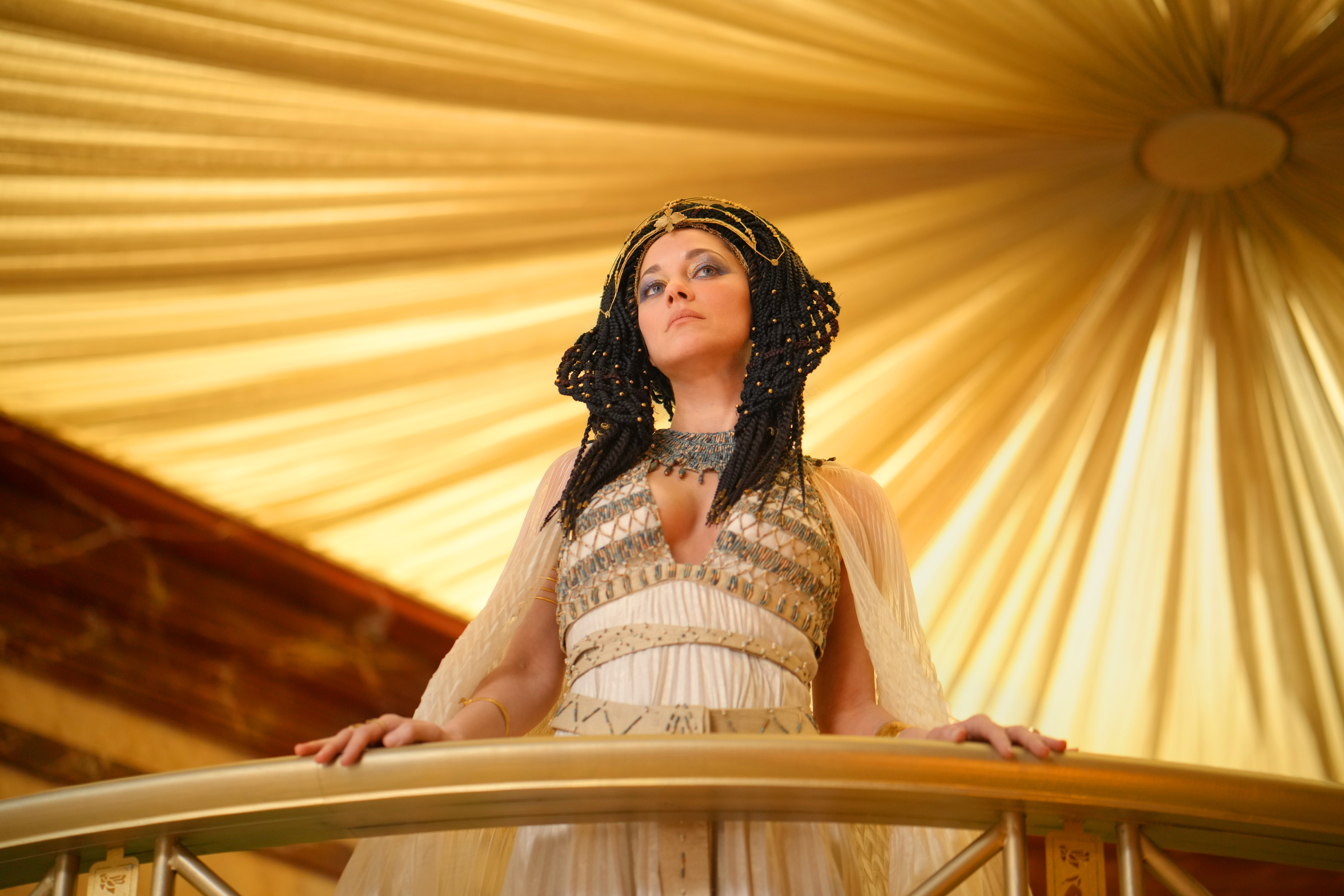 Frau in goldener Robe steht auf einem goldenen Balkon.