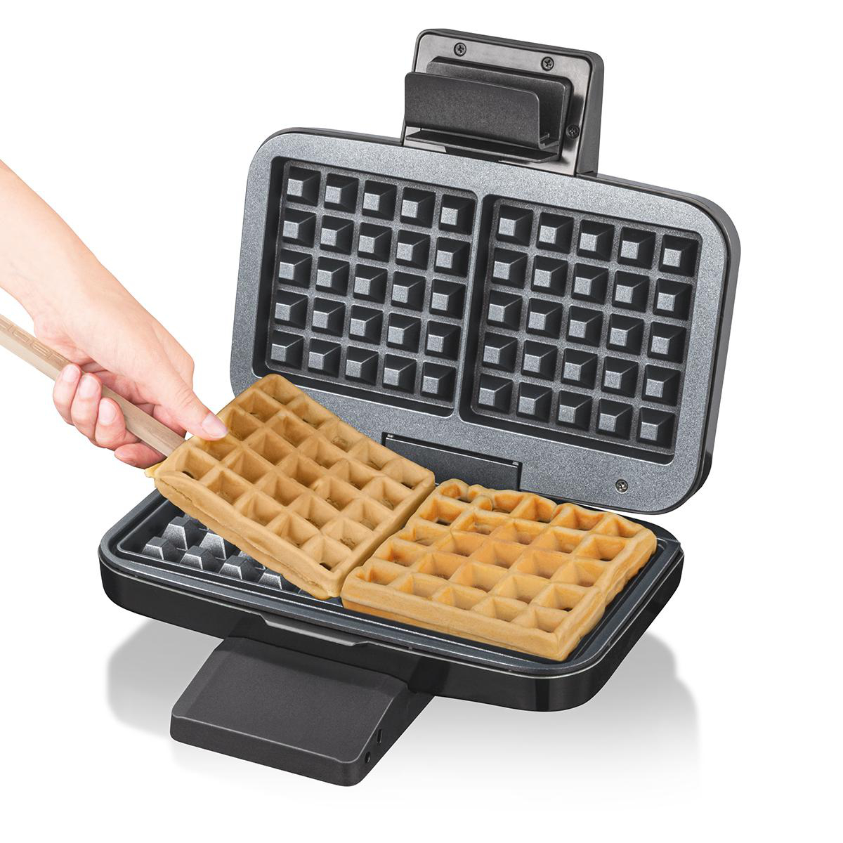 Waffeln werden aus einem Waffeleisen genommen. Eine Hand hält einen Spatel. Weißer Hintergrund.