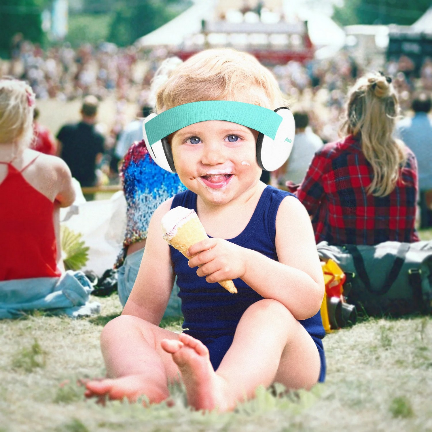 Un tout-petit portant un casque antibruit, mangeant un cornet de glace, souriant à la caméra.