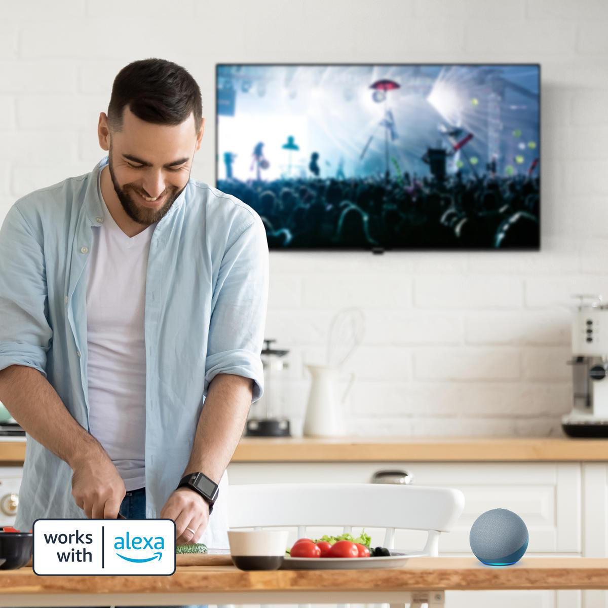 Mann in einer Küche, der Gemüse schneidet, mit Alexa-Lautsprecher und Fernseher im Hintergrund.