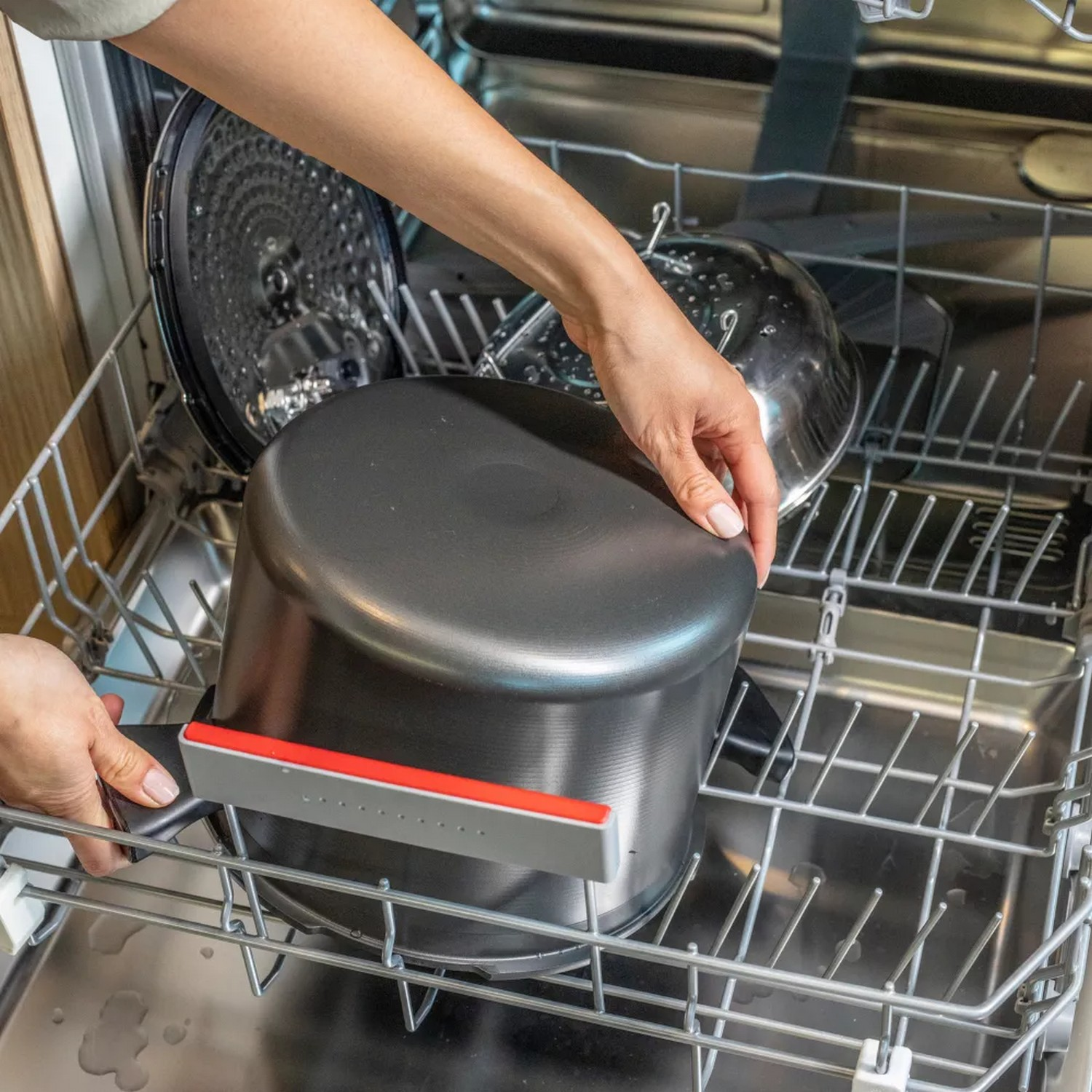 Person putting a pot in a dishwasher. Silver and black pot.