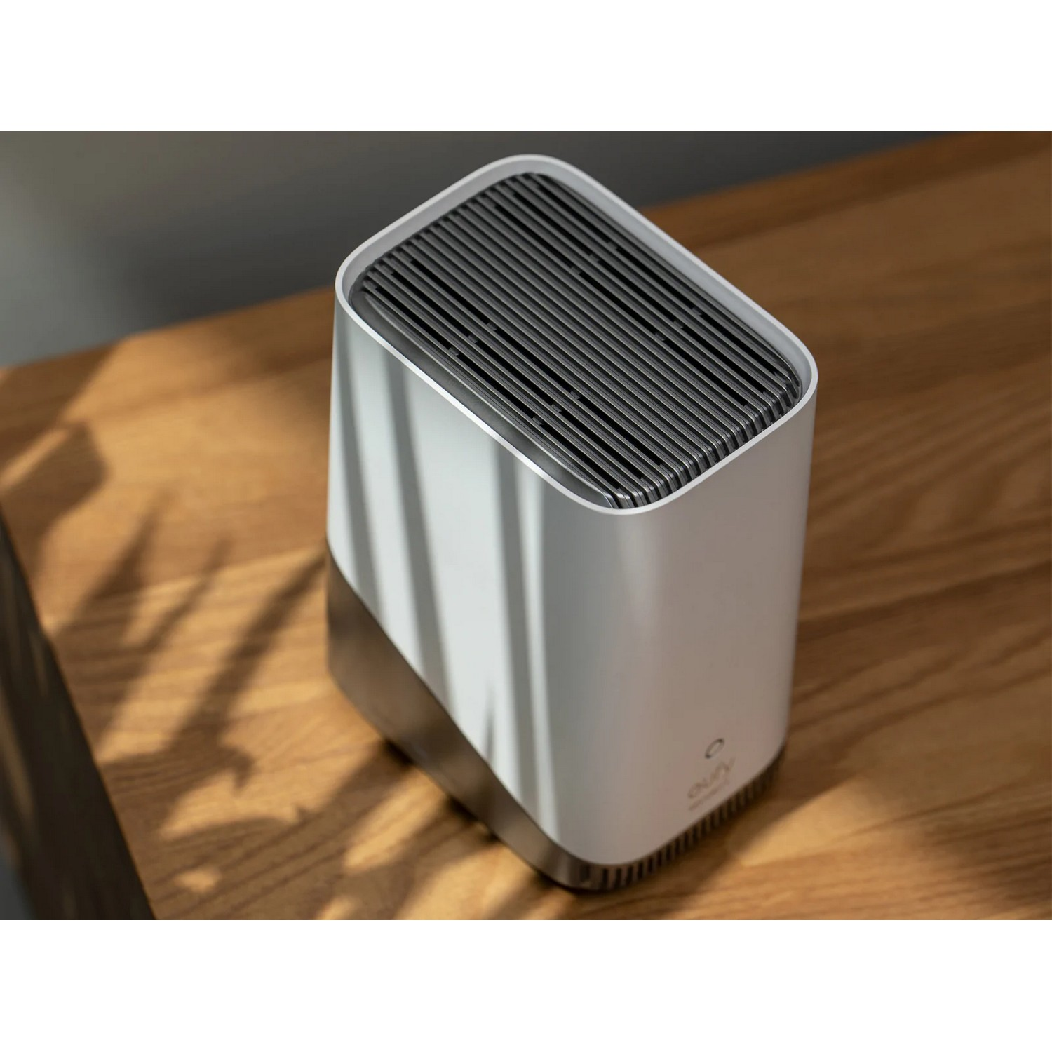 Un purificateur d'air rectangulaire blanc. Il est posé sur une table en bois. Il a un dessus sombre.