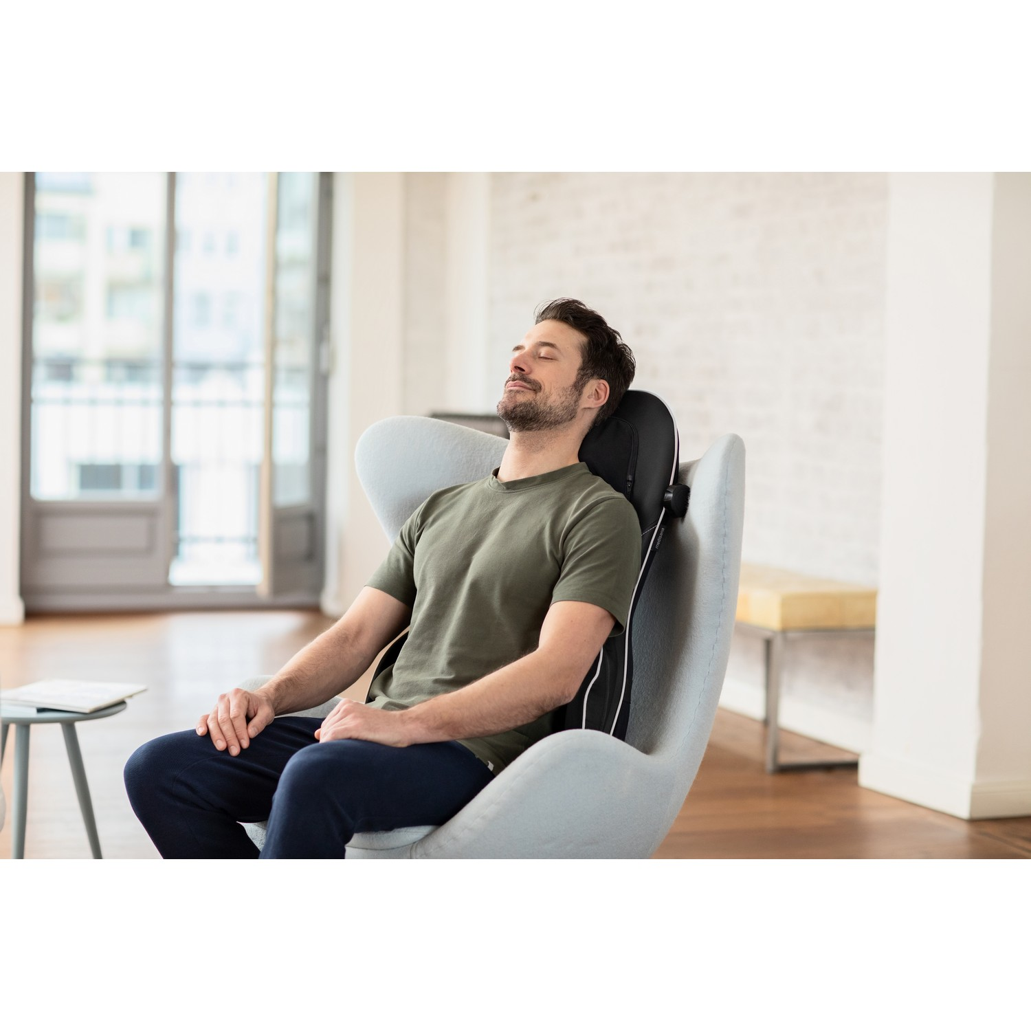 A man is sitting in a grey chair with his eyes closed. There is a head and back support.