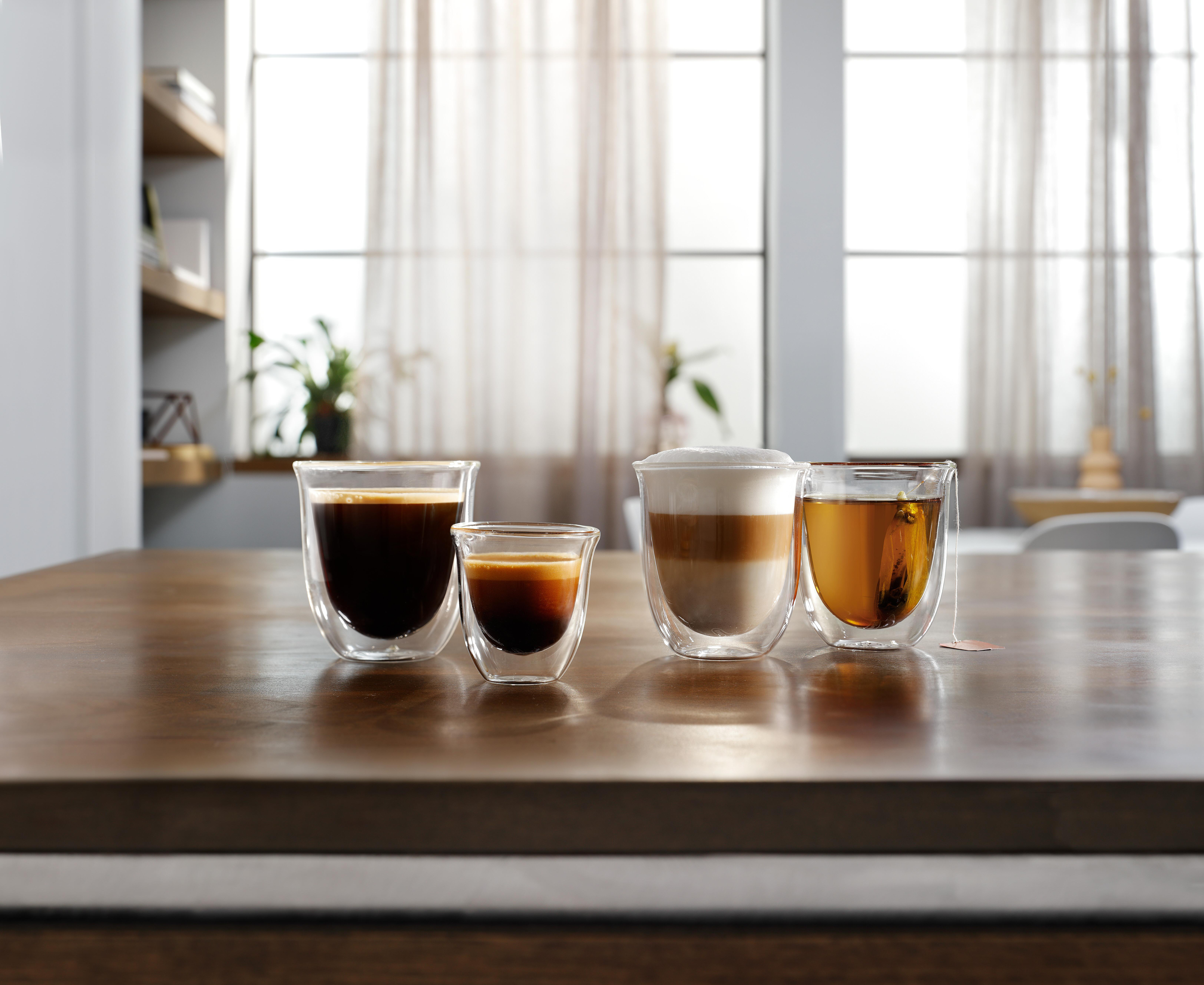 Vier Glasbecher mit Kaffee und Tee auf einem Holztisch. Licht fällt durch ein Fenster.