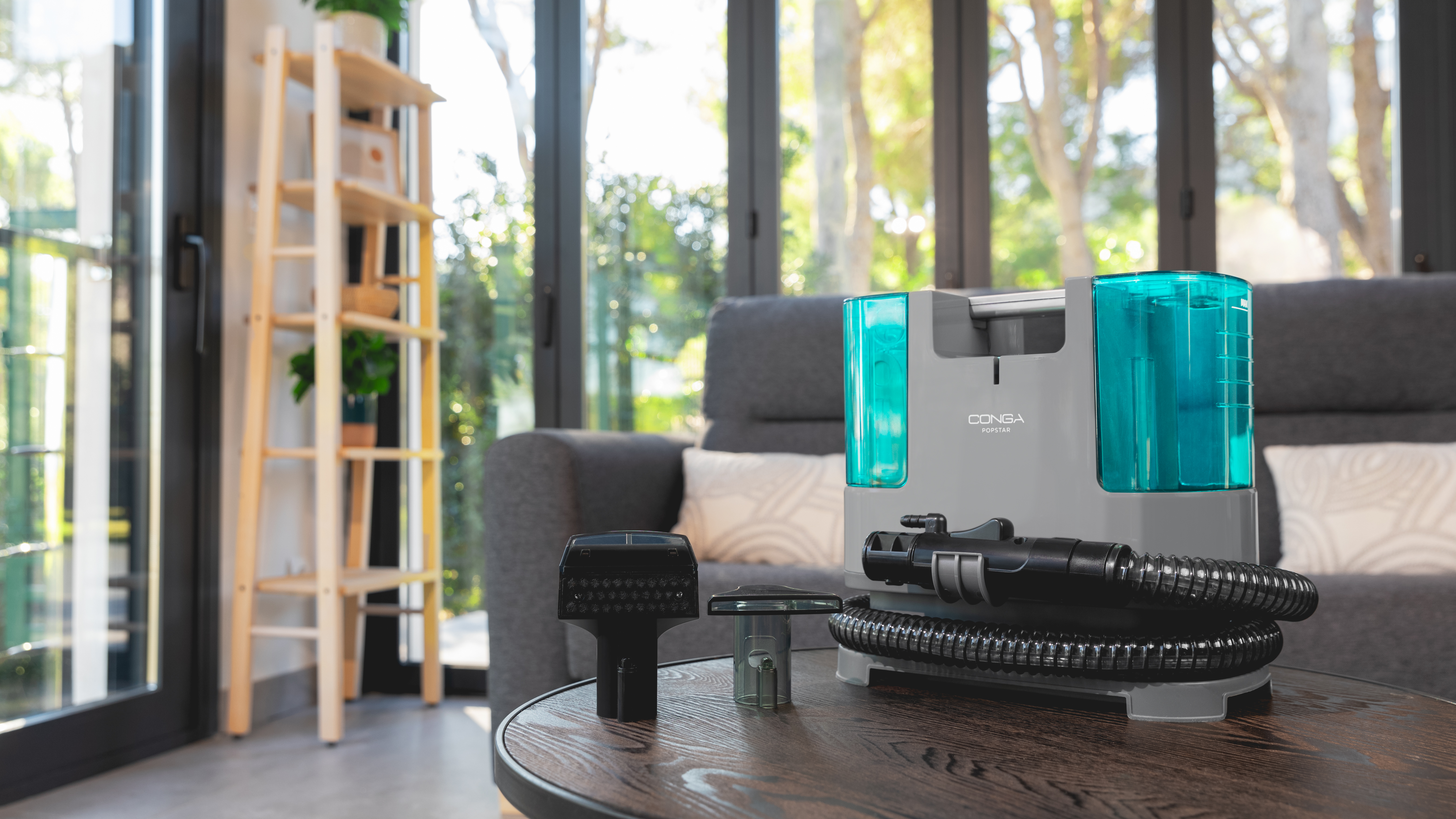 Máquina de limpieza gris con accesorios sobre una mesa y ventana al fondo.