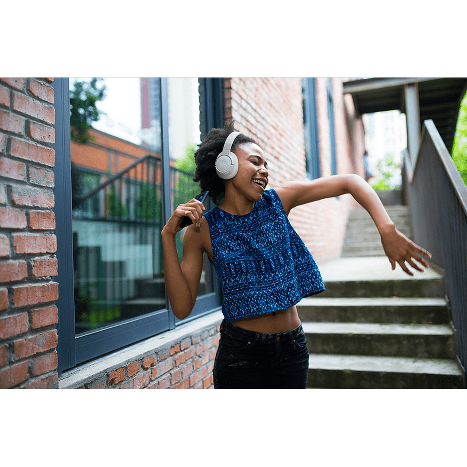 Woman dancing, wearing headphones, in city setting.