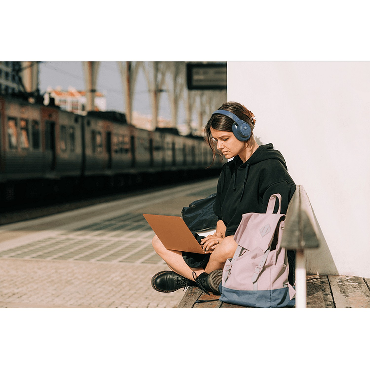 Femme avec casque et ordinateur portable assise sur un banc, train en arrière-plan.