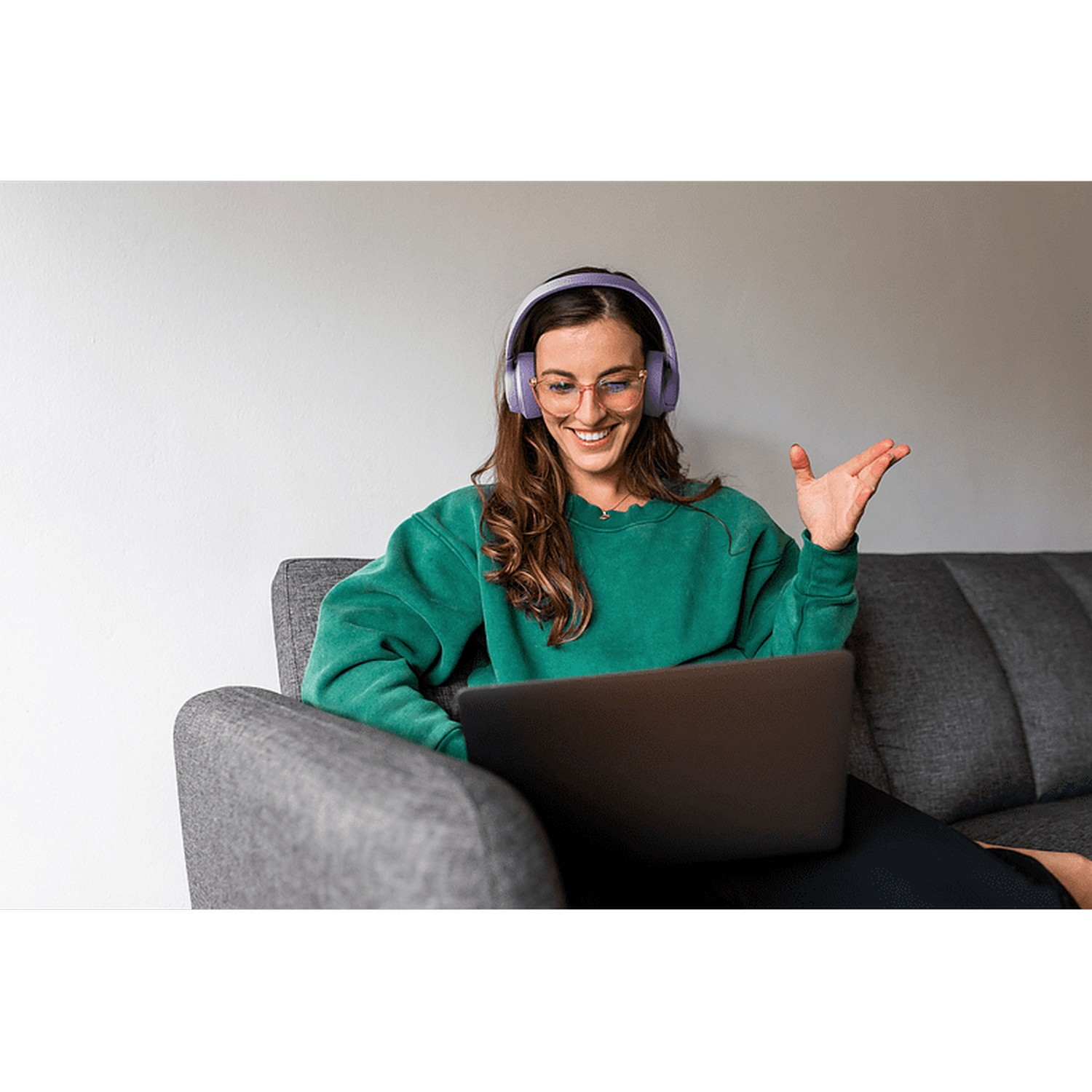 Femme avec des lunettes et un casque utilisant un ordinateur portable sur un canapé.