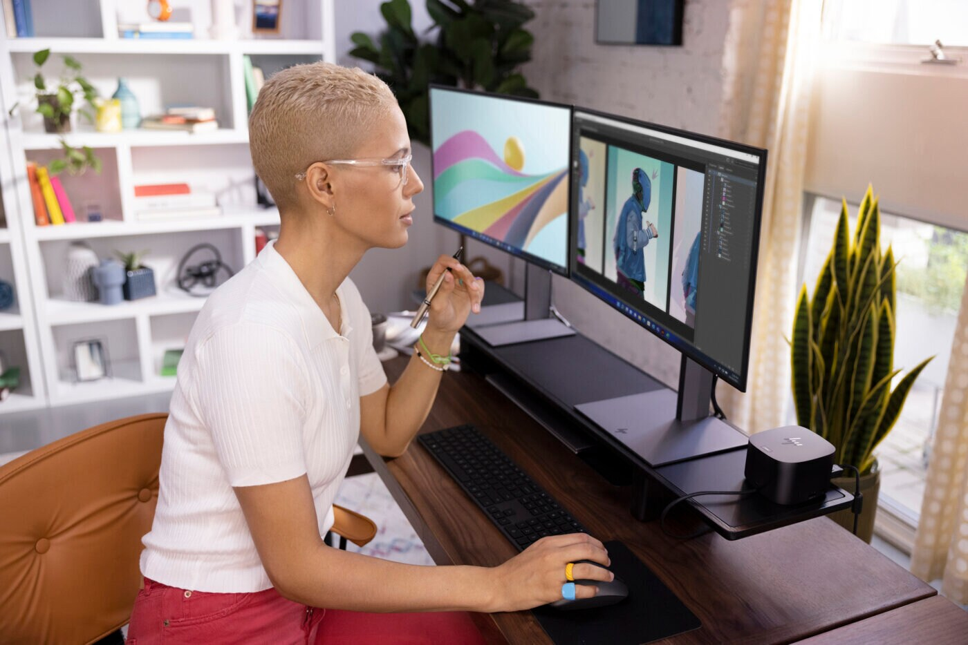 Woman working on a computer, with two screens and a plant.