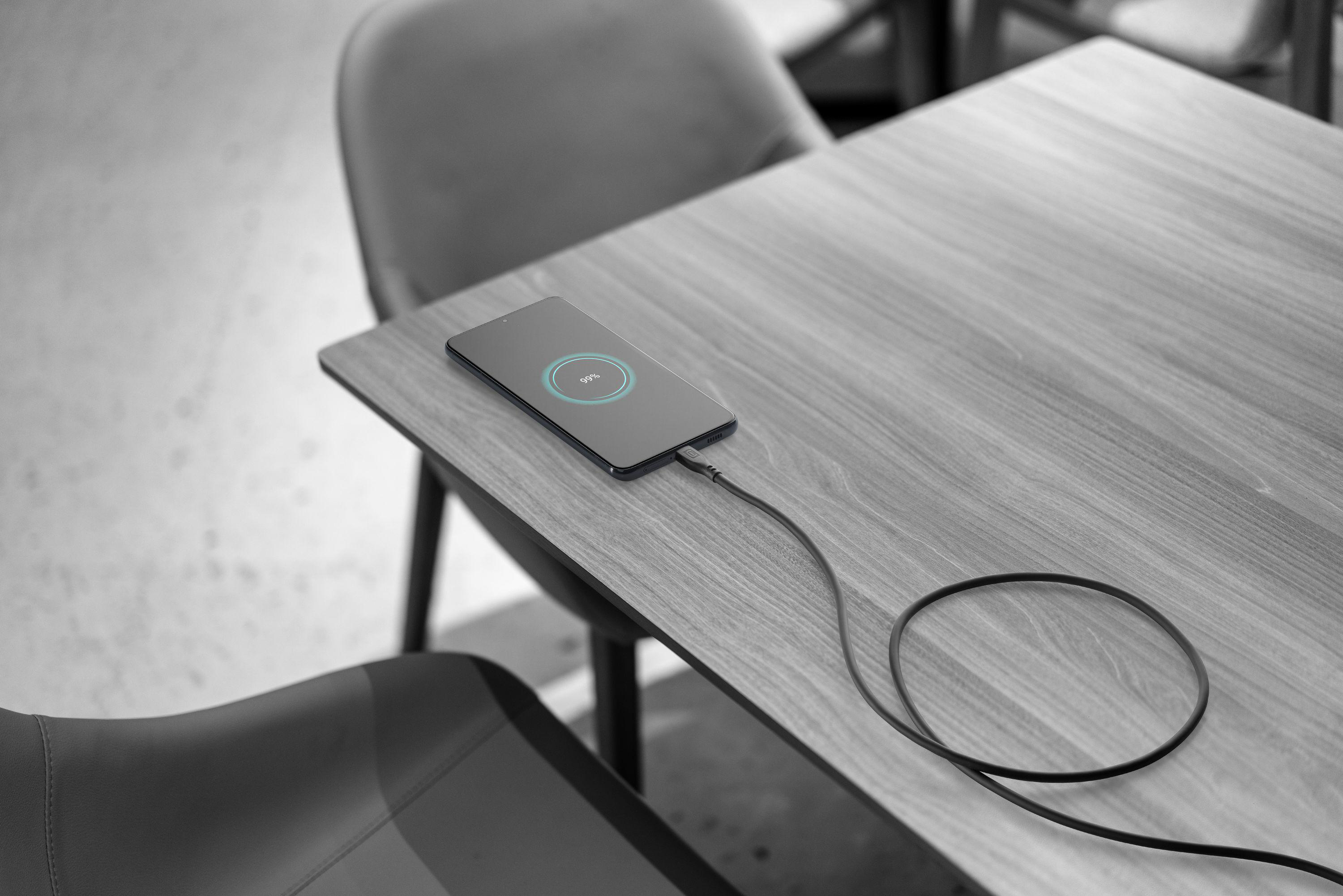Ein Smartphone, das auf einem Holztisch mit einem Ladekabel geladen wird.
