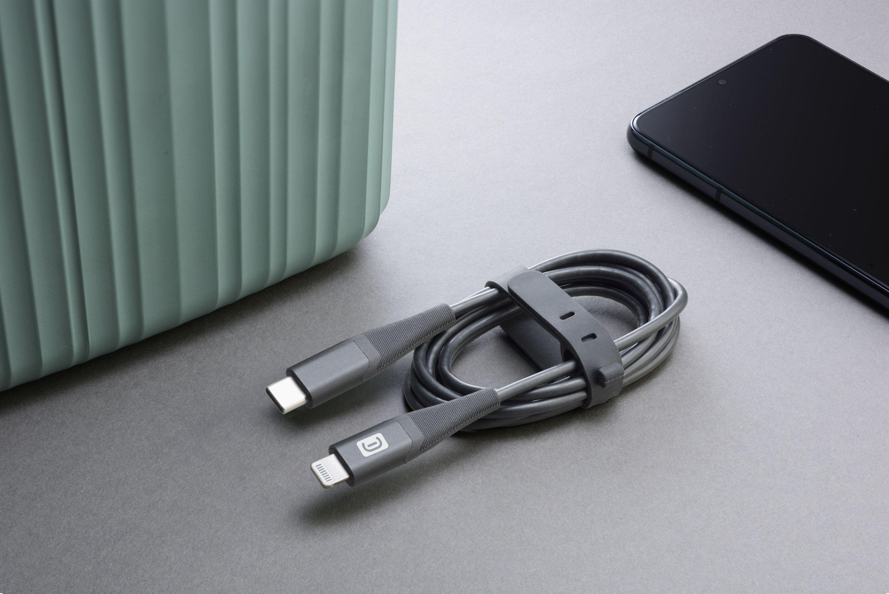 Zwei Ladekabel mit USB-C- und Lightning-Anschlüssen, neben einem Telefon und einem grünen Behälter.