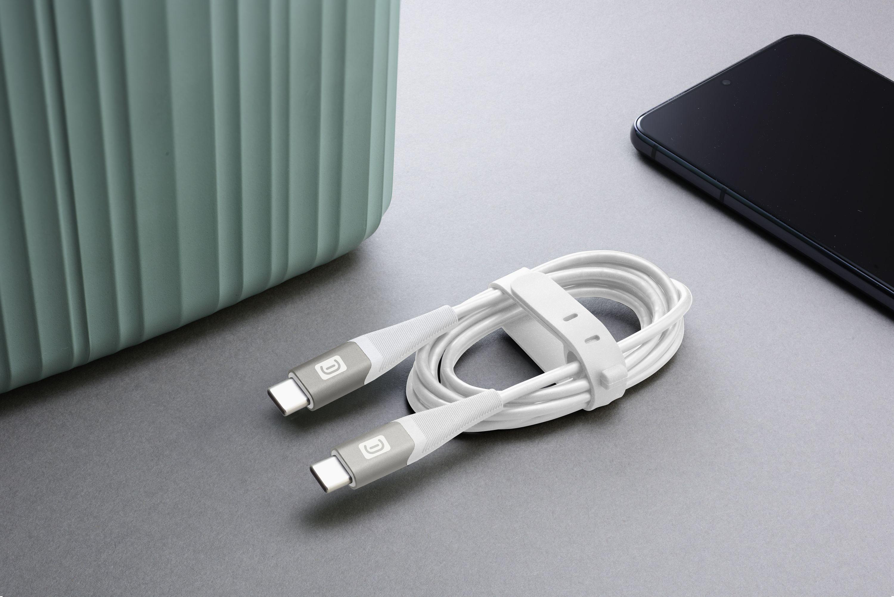 Weißes USB-C-Kabel aufgerollt, gehalten von einem weißen Riemen, neben einer grünen Box und einem schwarzen Telefon.