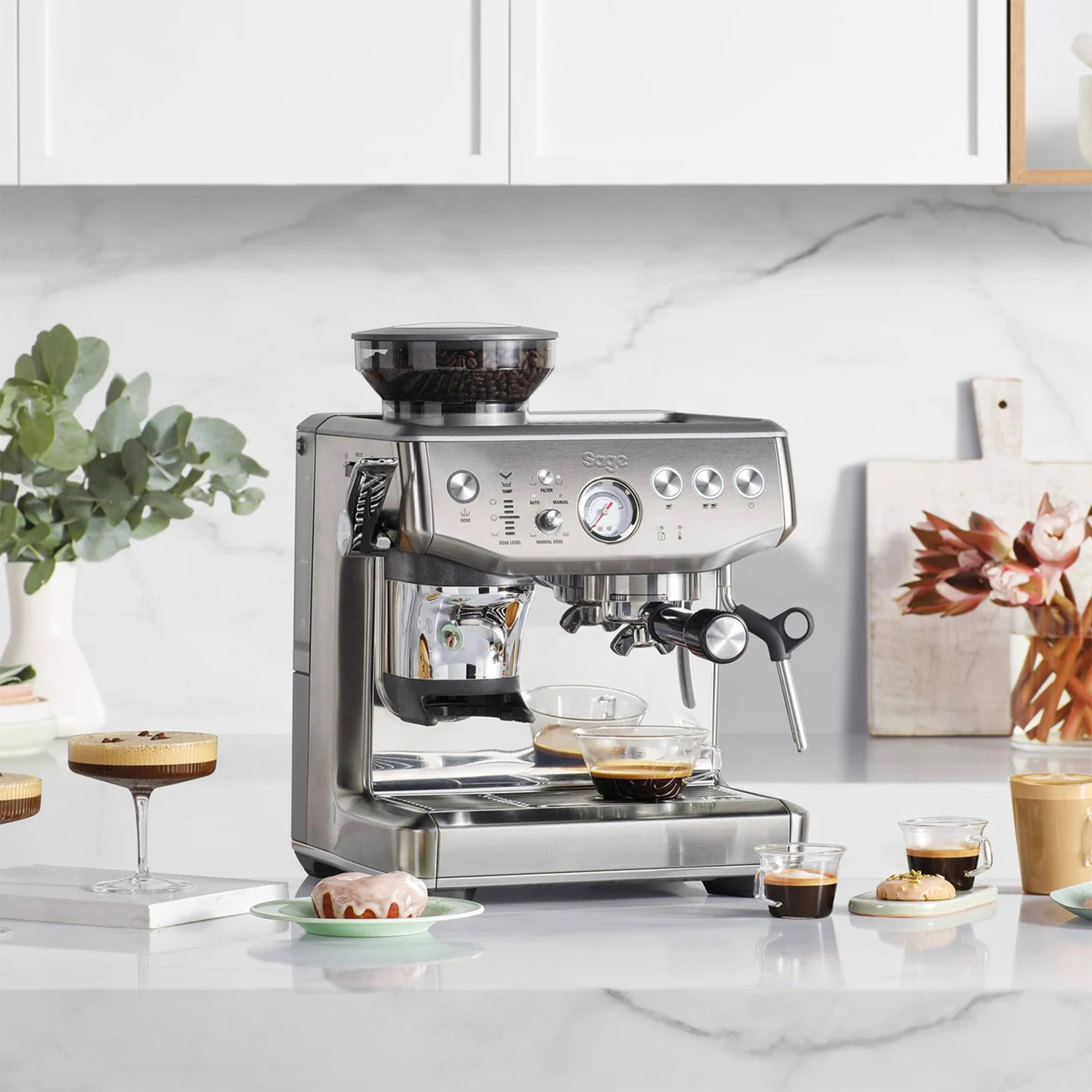 Macchina per caffè espresso argentata con accessori. Tazzine da caffè e un dolce sul bancone.