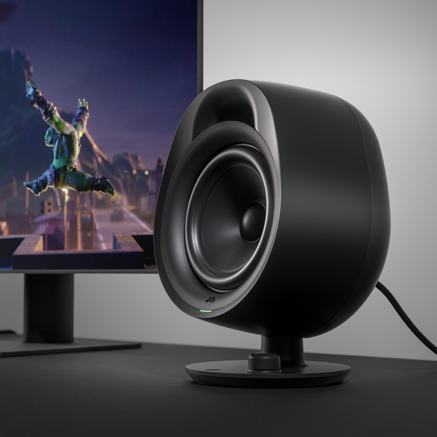 A black speaker with a green light on a stand.