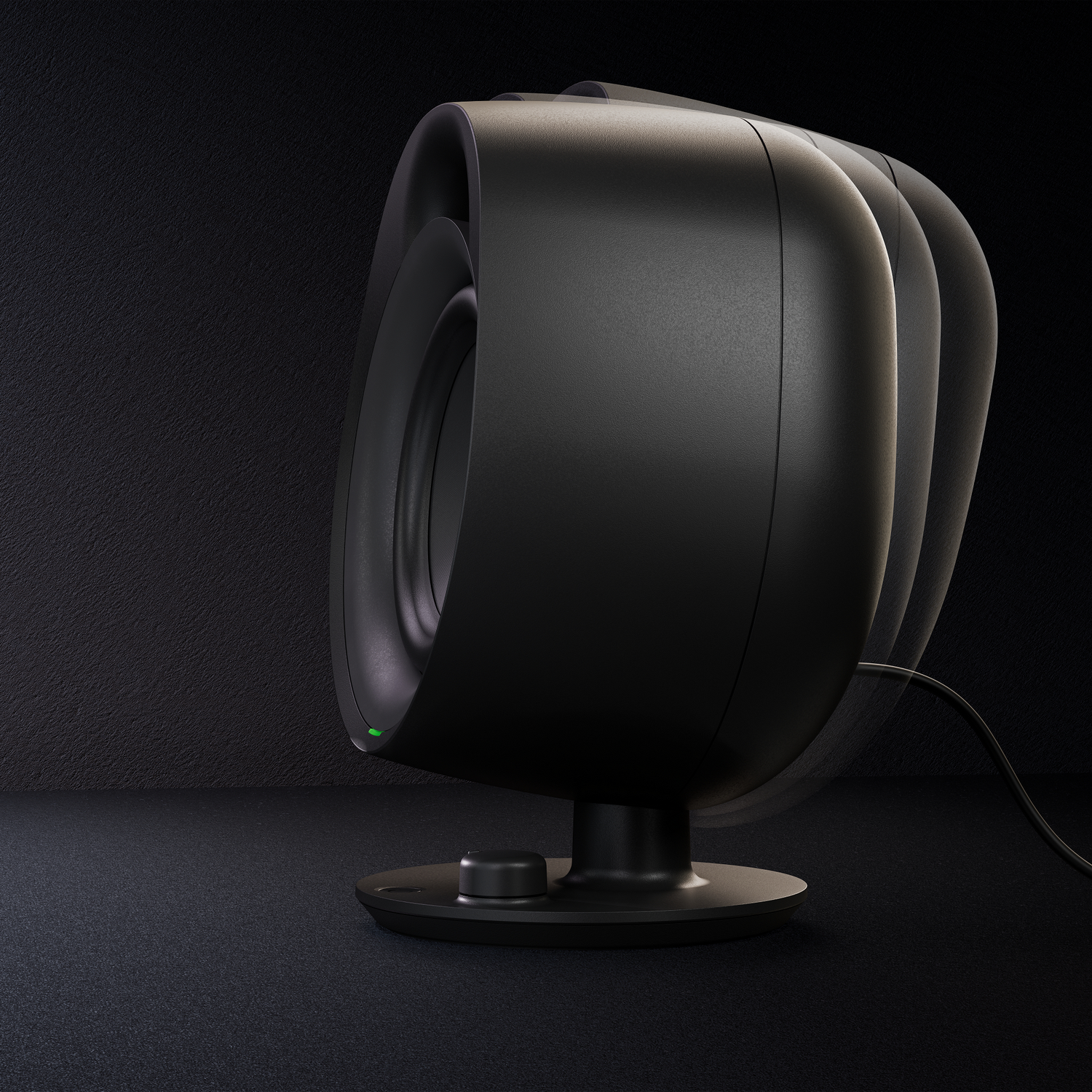 Black speaker with a green light. The speaker is on a dark surface, with a dark background.