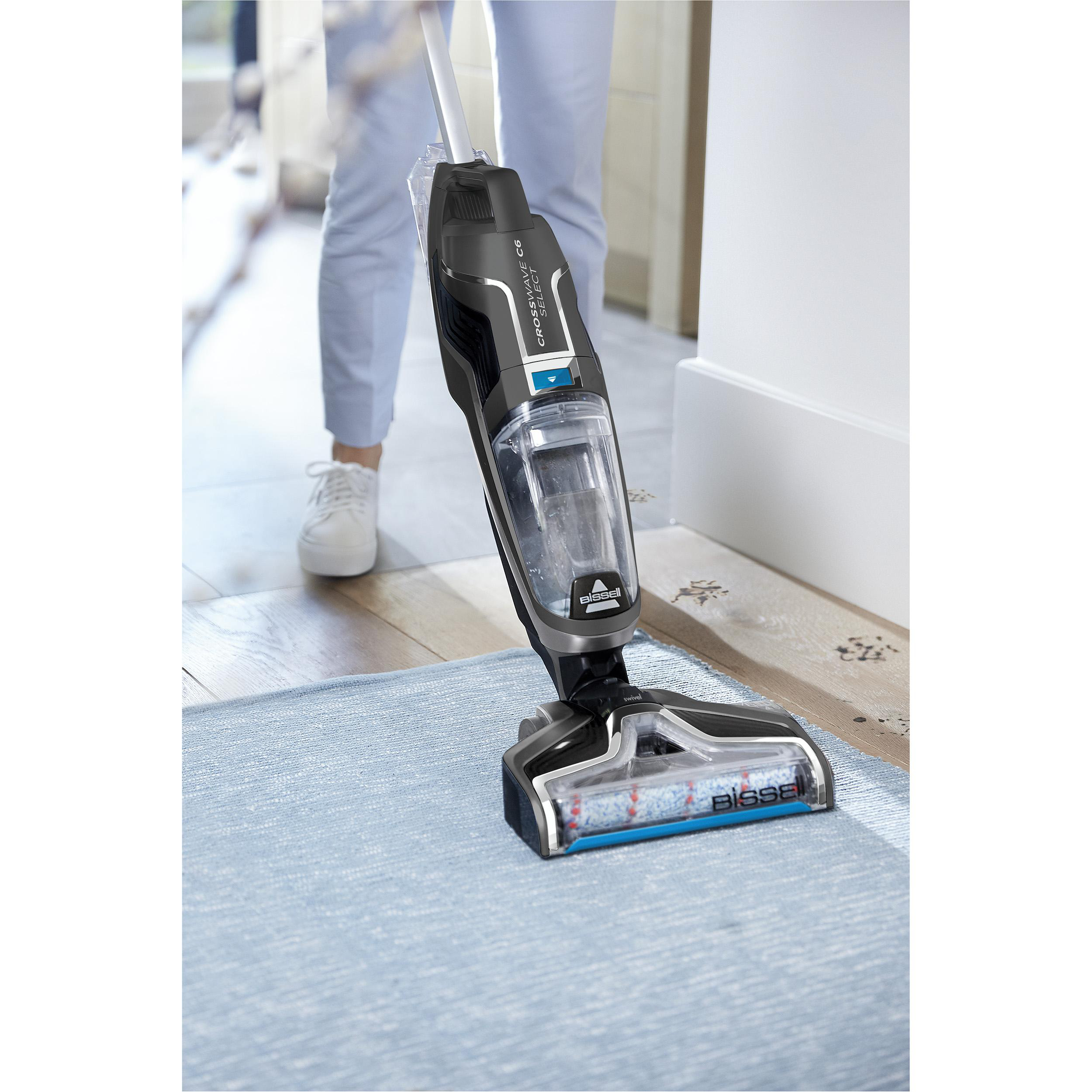 Person saugt einen blauen Teppich mit einem schwarz-silbernen Staubsauger.