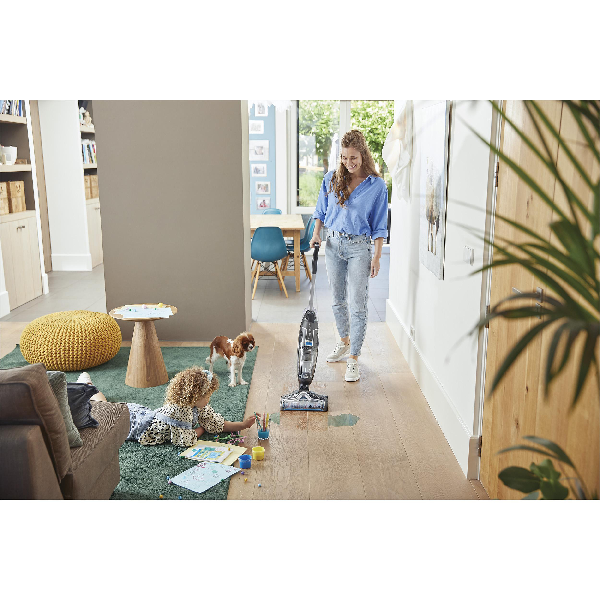Frau saugt, Kind zeichnet, Hund in hellem Raum.