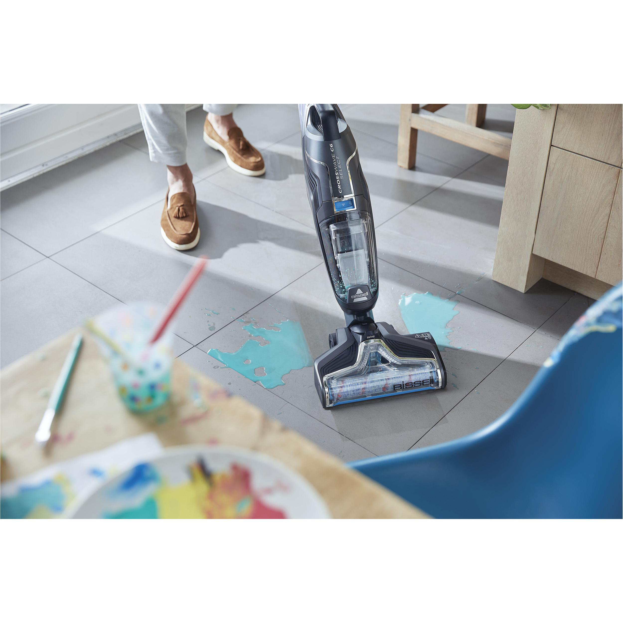 Eine Person verwendet einen Bissell CrossWave Staubsauger, um verschüttete blaue Flüssigkeit auf einem Fliesenboden zu reinigen.
