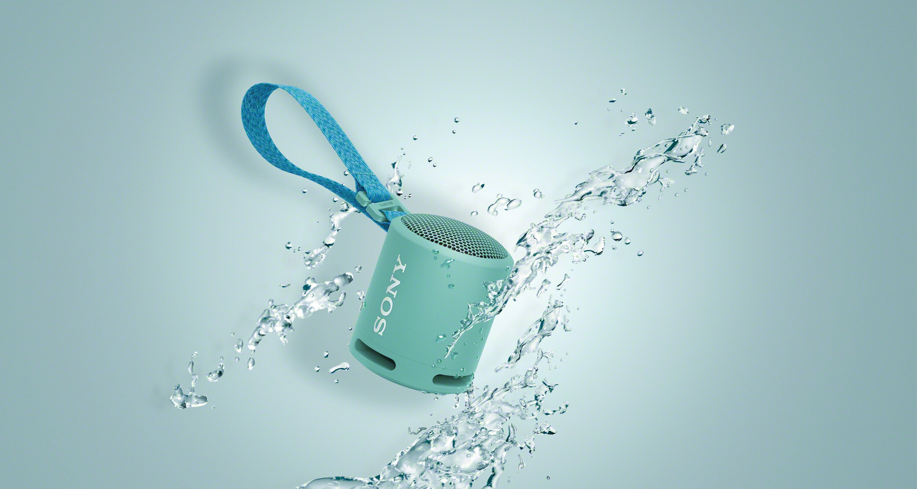 Mały, turkusowy głośnik emitujący rozpryski wody, z niebieskim paskiem.