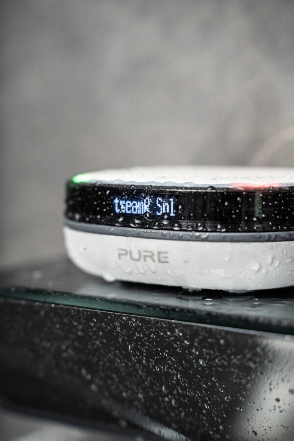 Biało-czarne urządzenie z cyfrowym wyświetlaczem pokazującym tekst, otoczone kroplami wody.