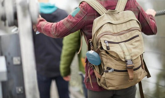 Osoba z plecakiem trzyma niebieski głośnik.