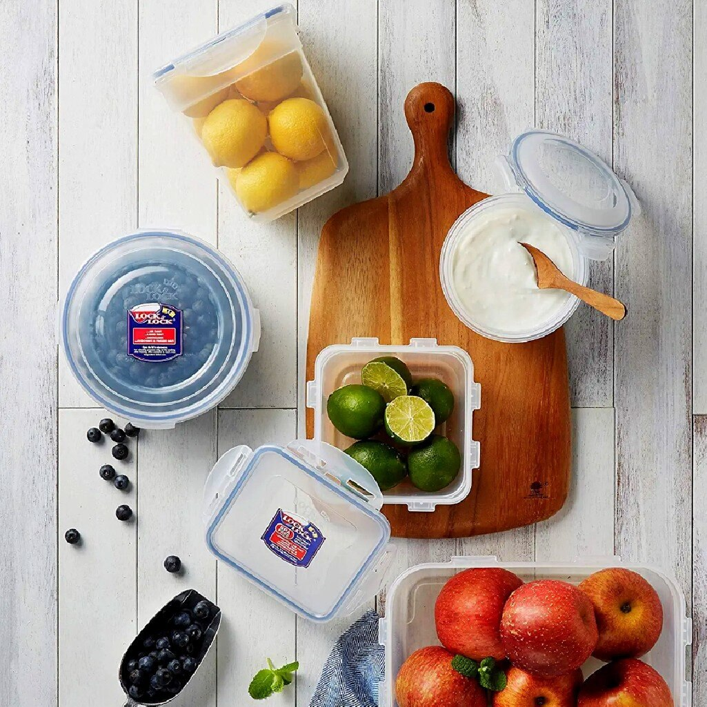 Pojemniki na żywność z cytrynami, jagodami, limonkami, jogurtem i jabłkami na desce.