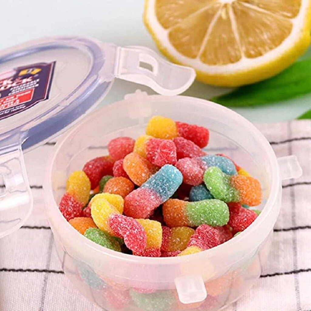 Przezroczysty pojemnik z kolorowymi żelkami. Cytryna i pokrywka są w tle.