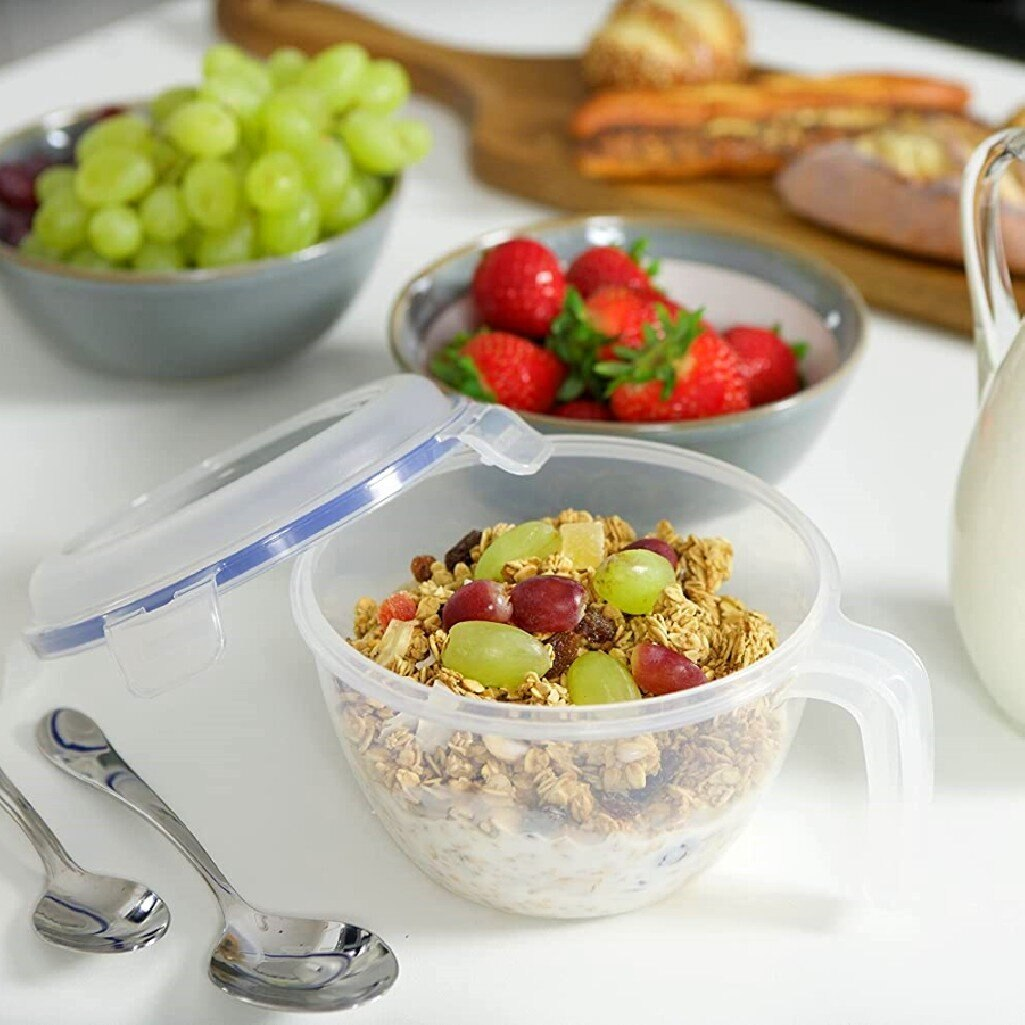 Miska granoli i owoców, z pokrywką, łyżkami i innymi miskami z owocami na białym stole.