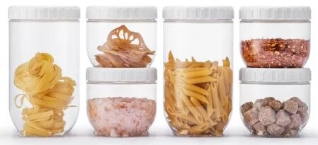 Szklane słoiki wypełnione produktami spożywczymi, takimi jak makaron, sól i przyprawy. Białe pokrywki na każdym słoiku.