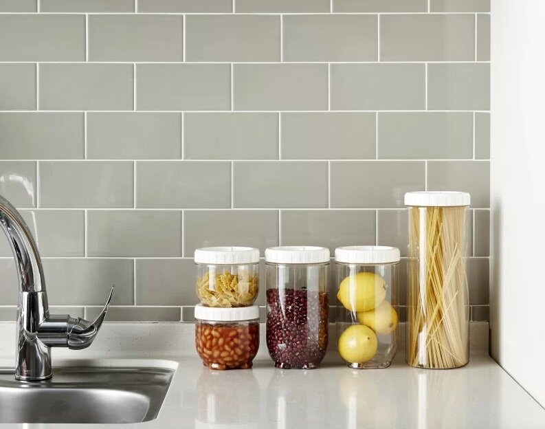 Blat kuchenny ze słoikami zawierającymi makaron, fasolę, cytryny i spaghetti. Tło to szara ściana z płytek.