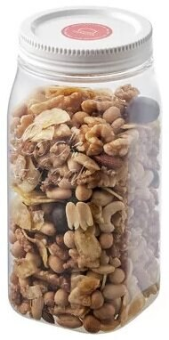 Przezroczysty słoik wypełniony różnymi orzechami i nasionami, na białym tle.