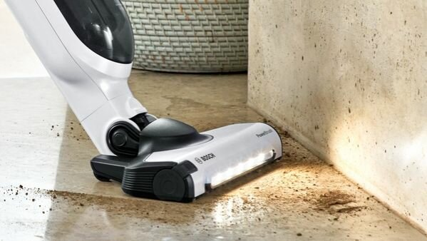 Biało-czarny odkurzacz czyszczący podłogę. Widoczny jest brązowy brud.