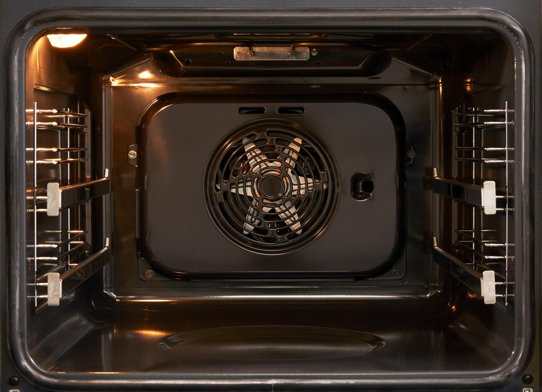 Ein Backofeninnenraum. Der Innenraum ist dunkel. Hinten ist ein Ventilator. An den Seiten sind Metallgestelle.