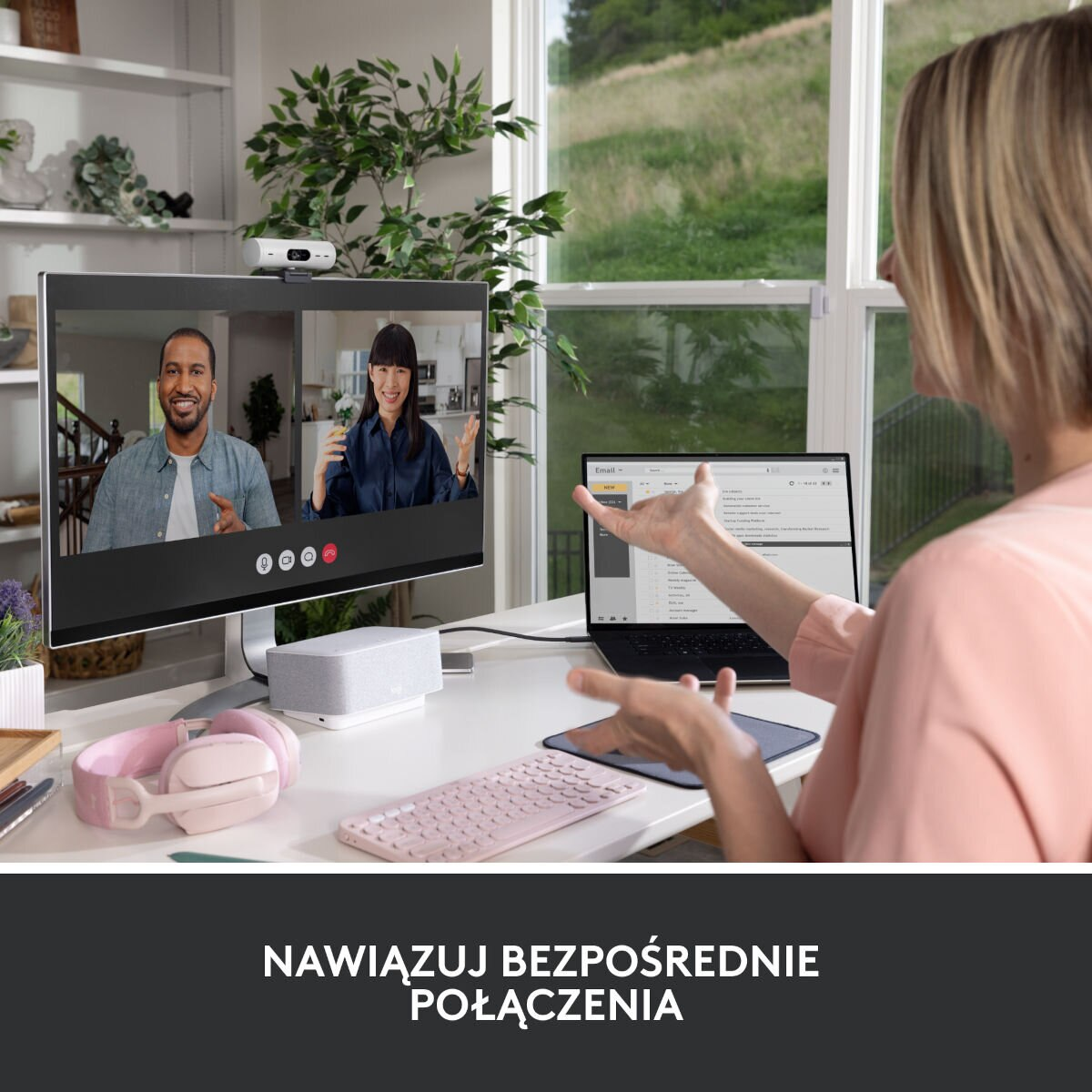 Kobieta przed monitorem z rozmową wideo, laptopem, różową klawiaturą i słuchawkami.