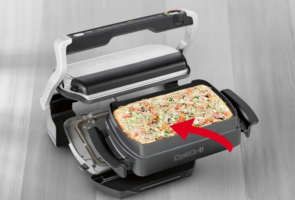 Otwarty grill z pizzą w środku. Grill stoi na drewnianej powierzchni.