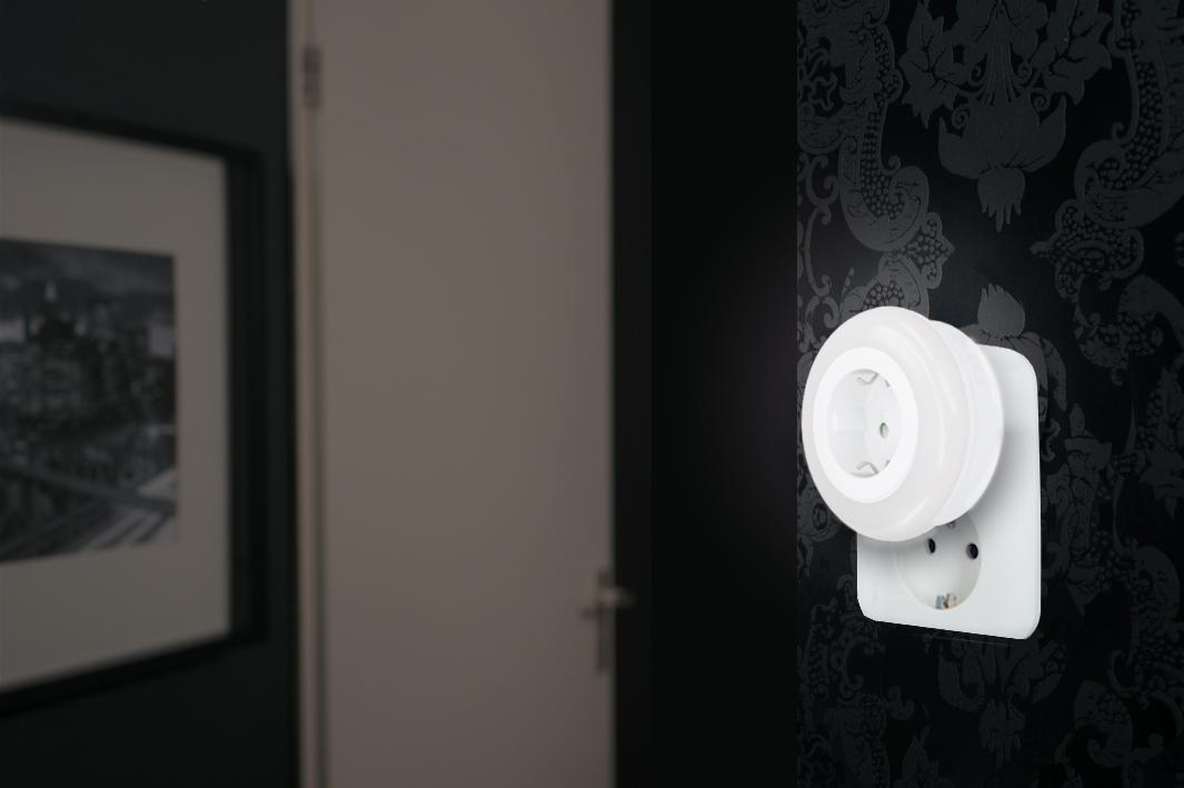 Ein weißes Nachtlicht in einer europäischen Steckdose auf einer schwarzen Tapete.