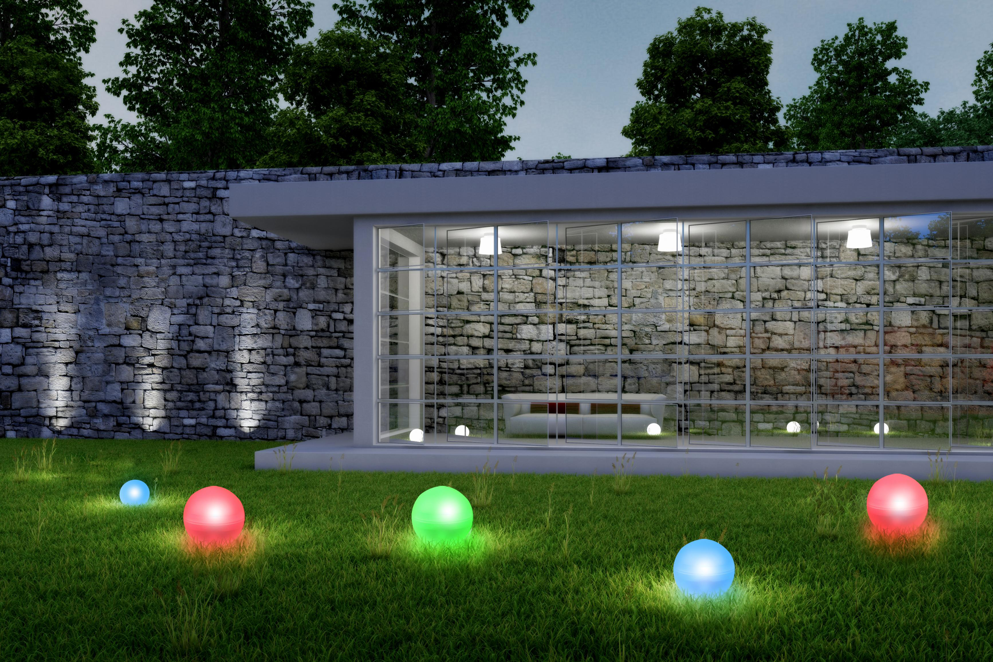 Modernes Gebäude mit Glaswänden, beleuchteten Kugeln auf Gras und Steinmauer im Hintergrund bei Nacht.