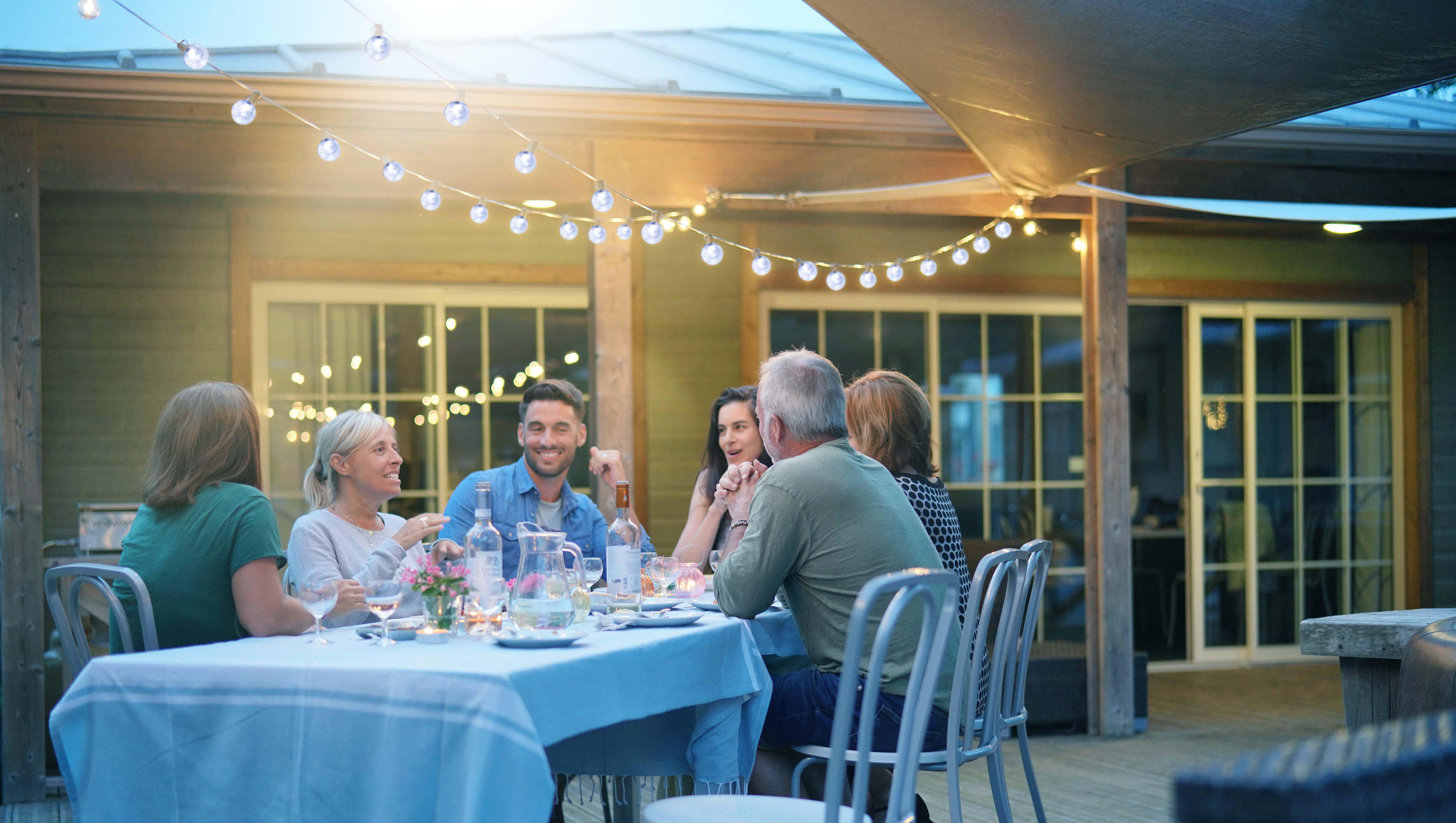 Gruppe von Leuten sitzt an einem Tisch, beleuchtet von Lichterketten im Freien bei Nacht.