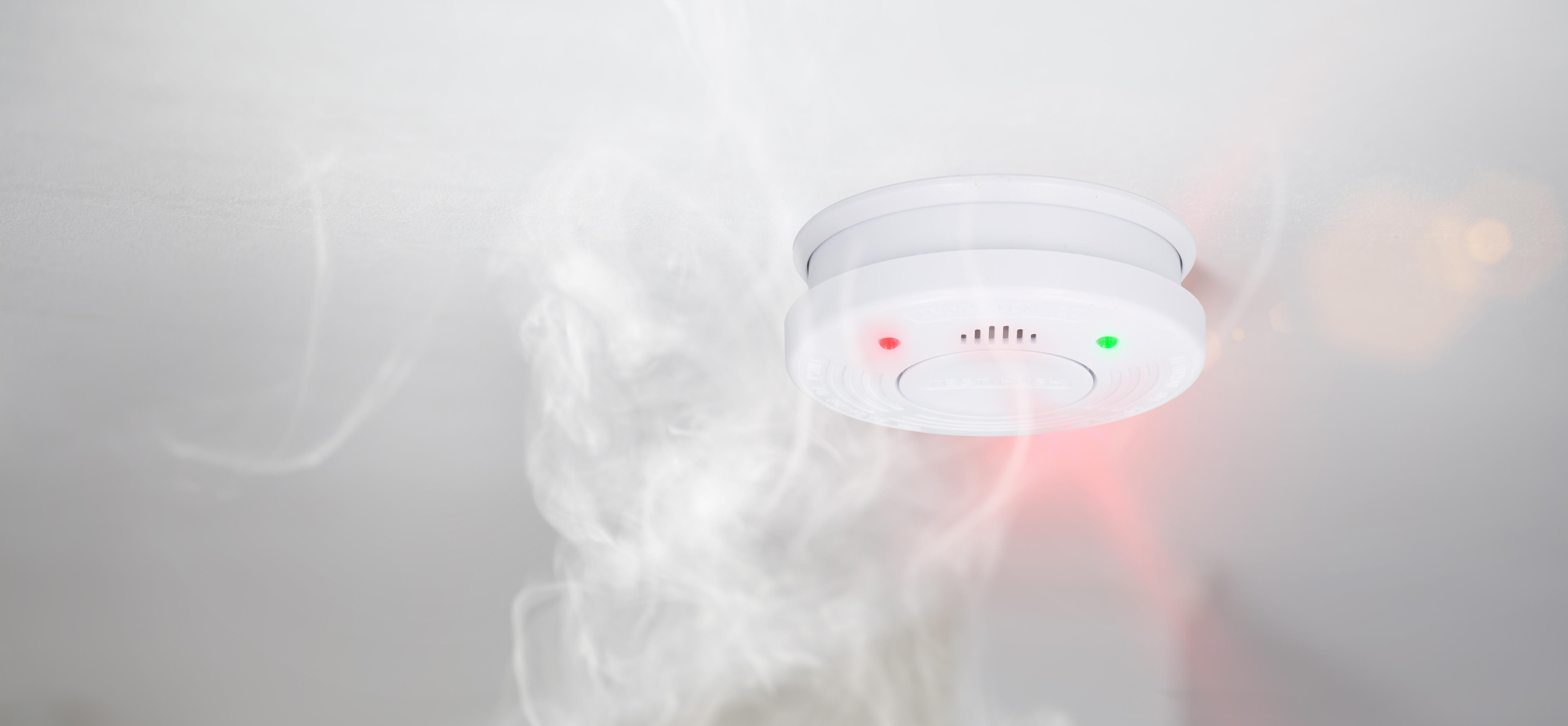 Weißer Rauchmelder an einer weißen Decke, mit roten und grünen Lichtern.