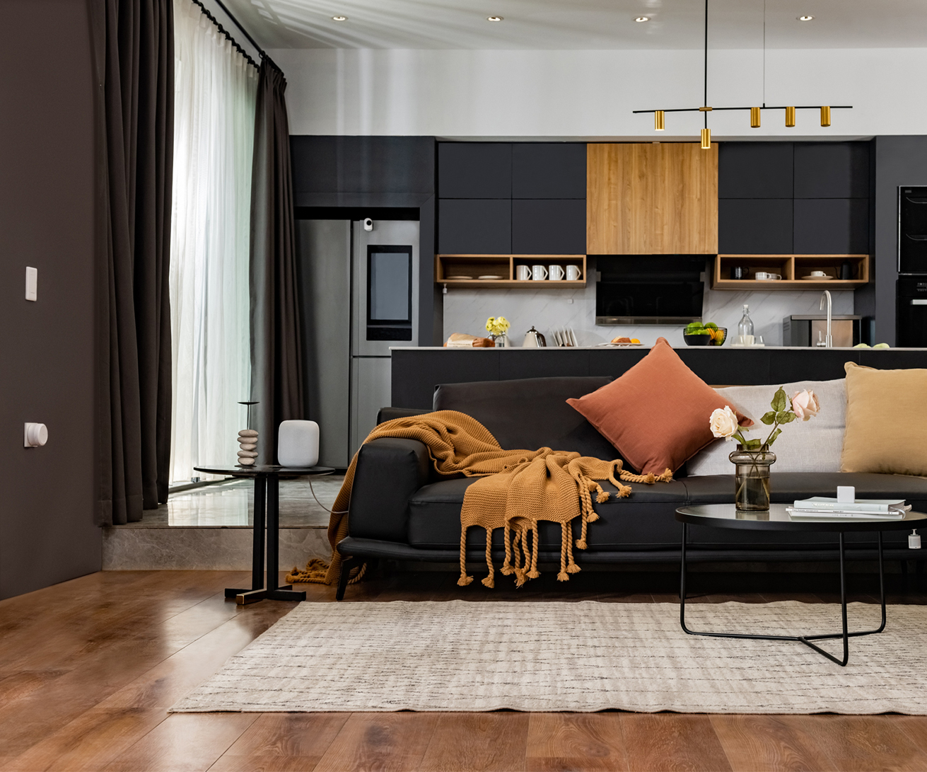 Salon moderne avec canapé noir, coin repas et cuisine en arrière-plan.