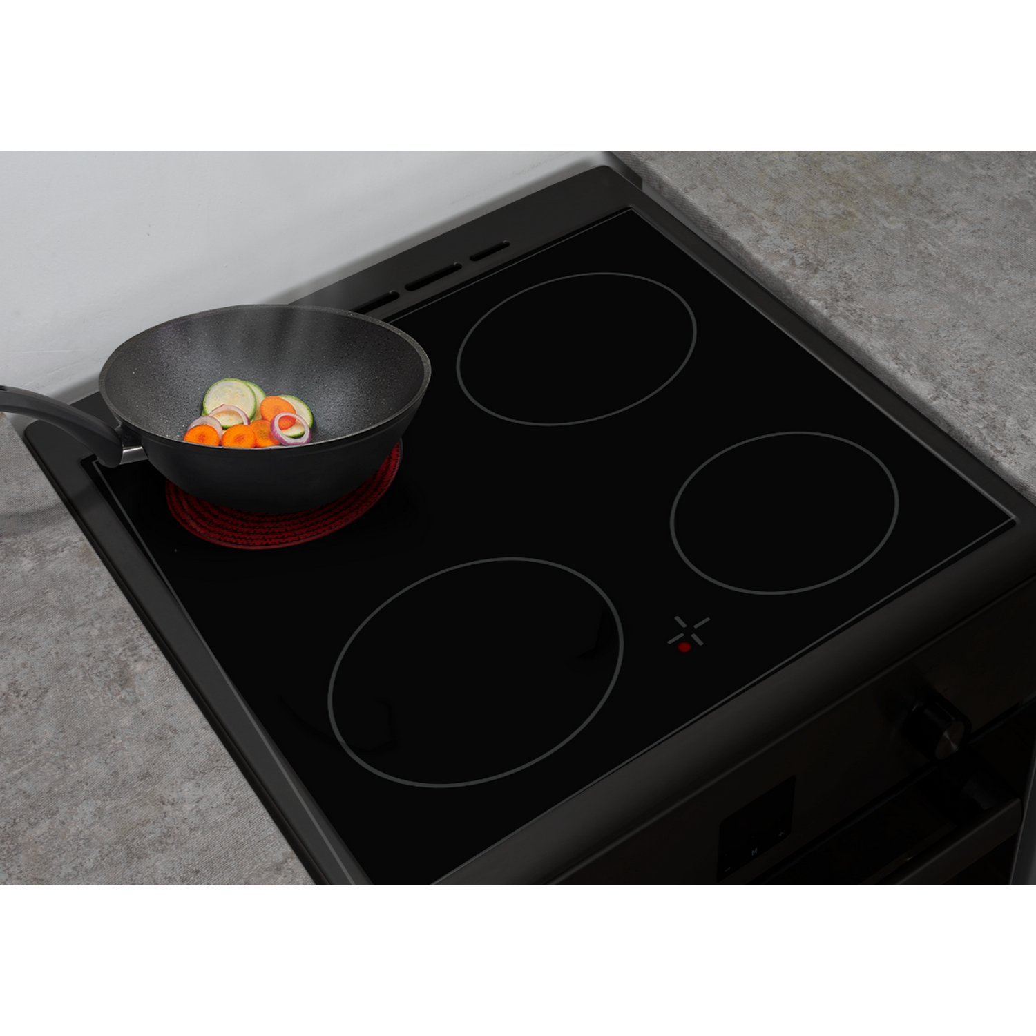 Une cuisinière électrique noire avec quatre brûleurs. Une poêle avec des légumes est sur l'un d'eux.