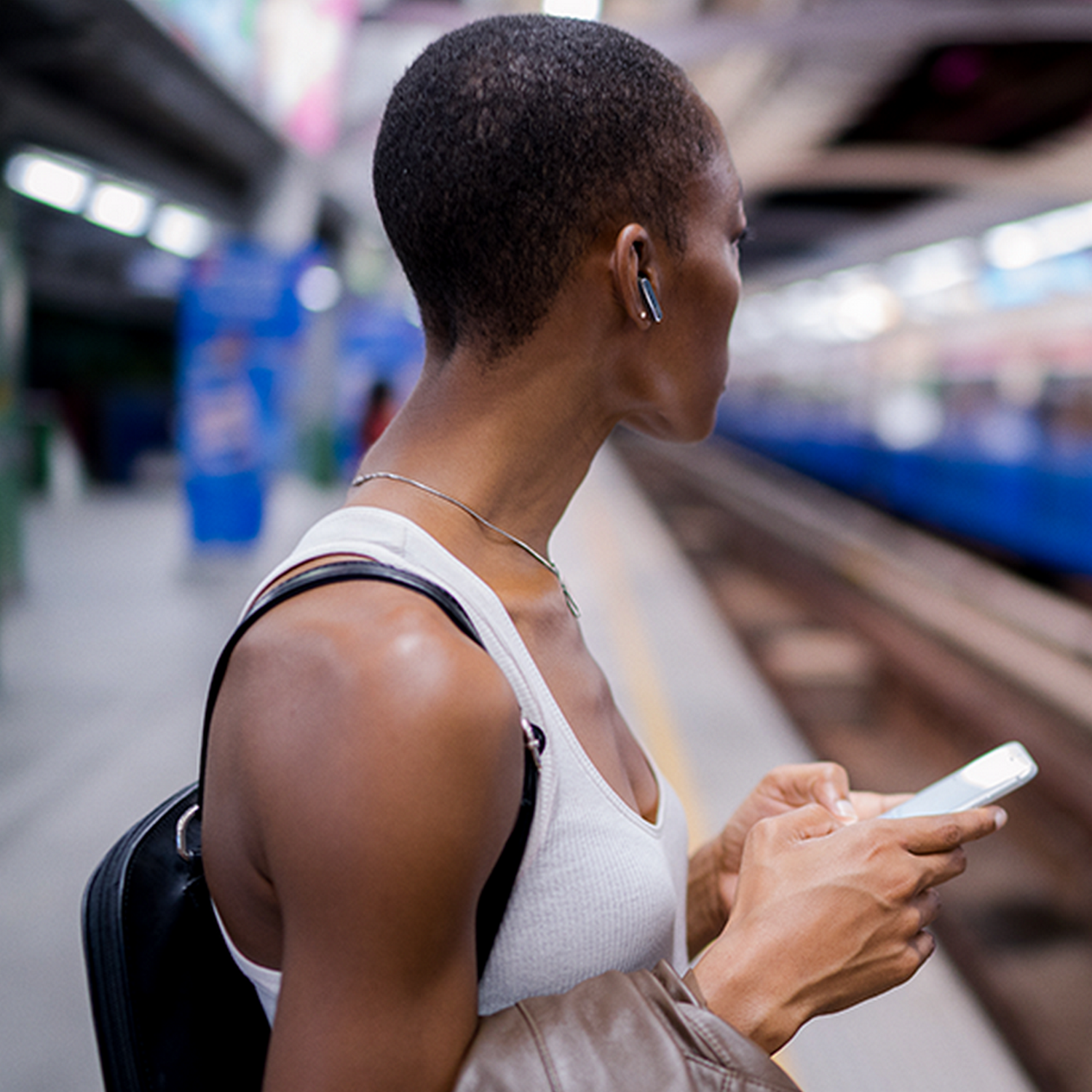 Woman wearing earbuds, looking away, using phone, at a station.