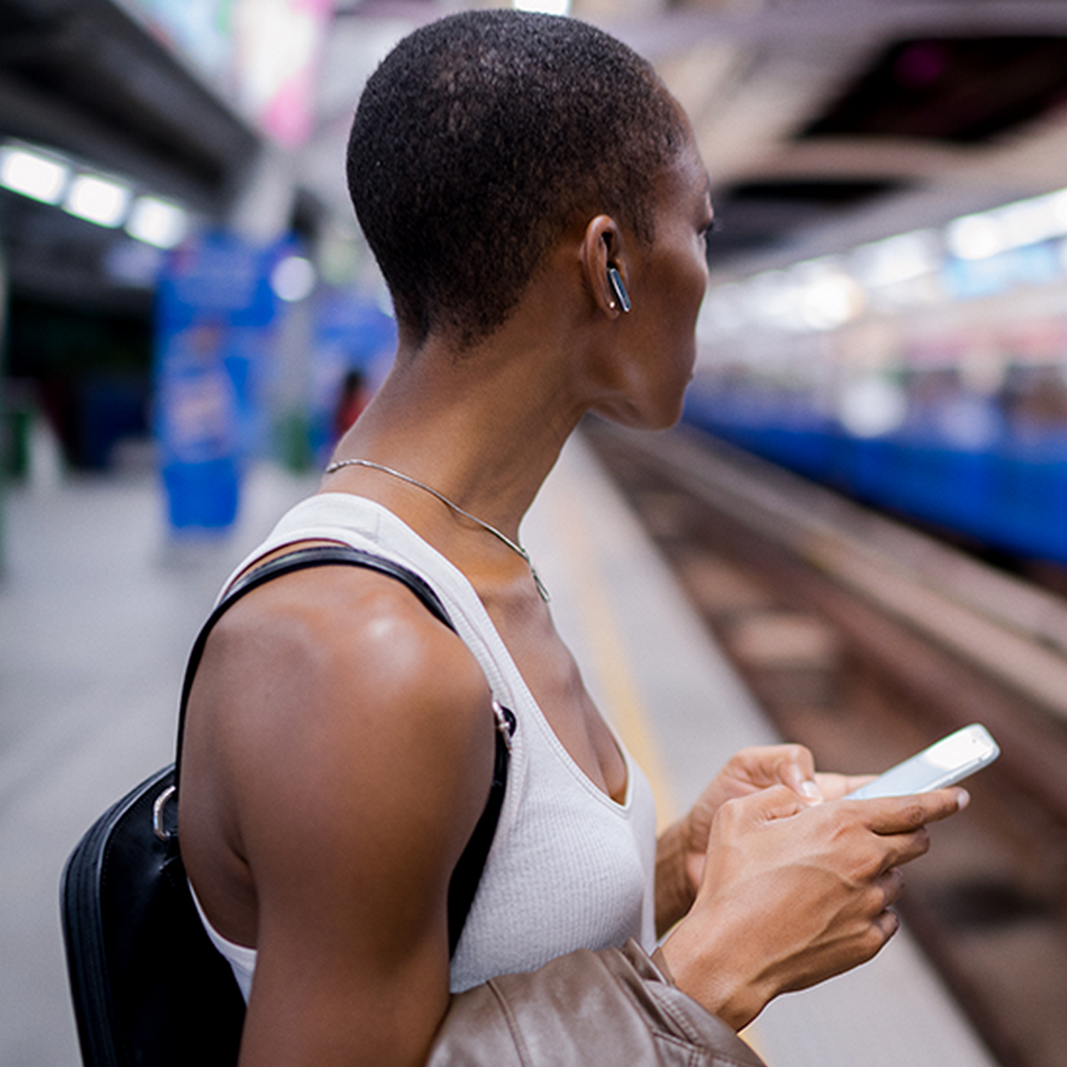 Woman at a train station holding a phone, wearing a white top and a backpack.